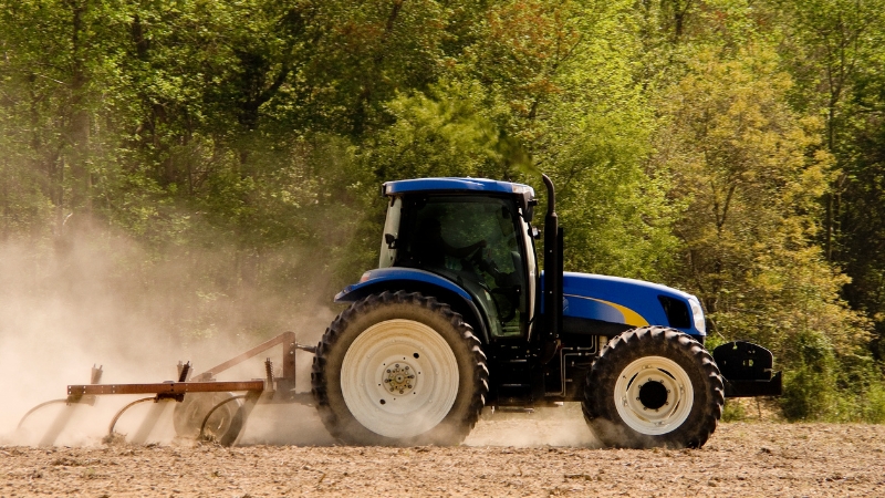 A blue tractor works a dusty field, highlighting features important for small farms