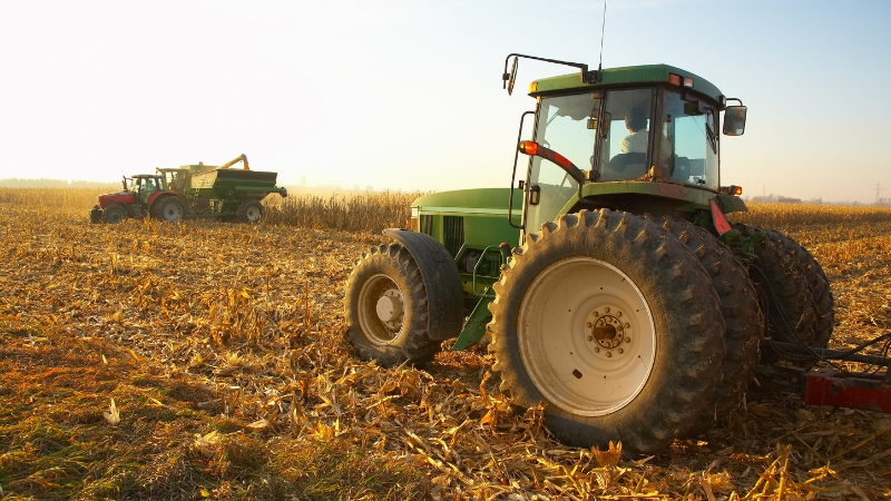 A green tractor works in a harvested cornfield, showing the equipment needs of mid-sized 50-acre farms