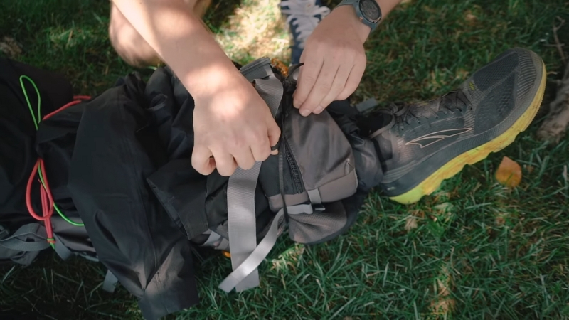 A person packing a backpack with emergency gear, including first aid supplies, on a grassy surface