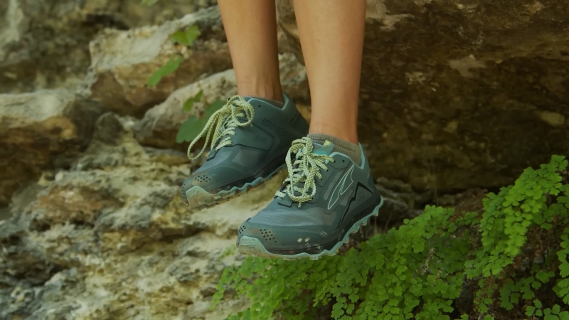A person wearing hiking shoes while perched on a rocky surface surrounded by greenery