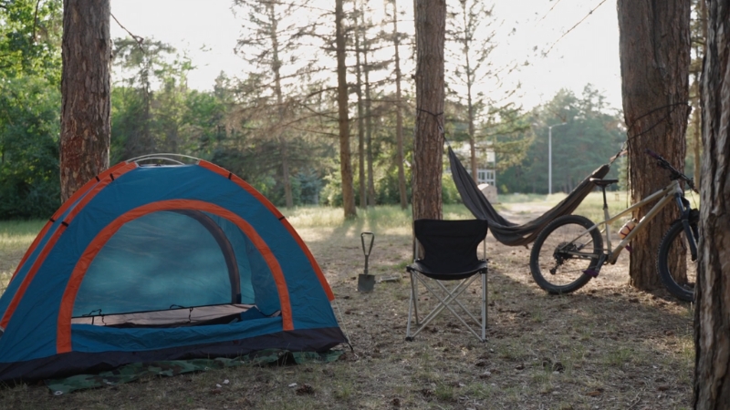 A camping setup featuring a tent, hammock, and outdoor chair next to a bike in a forested area